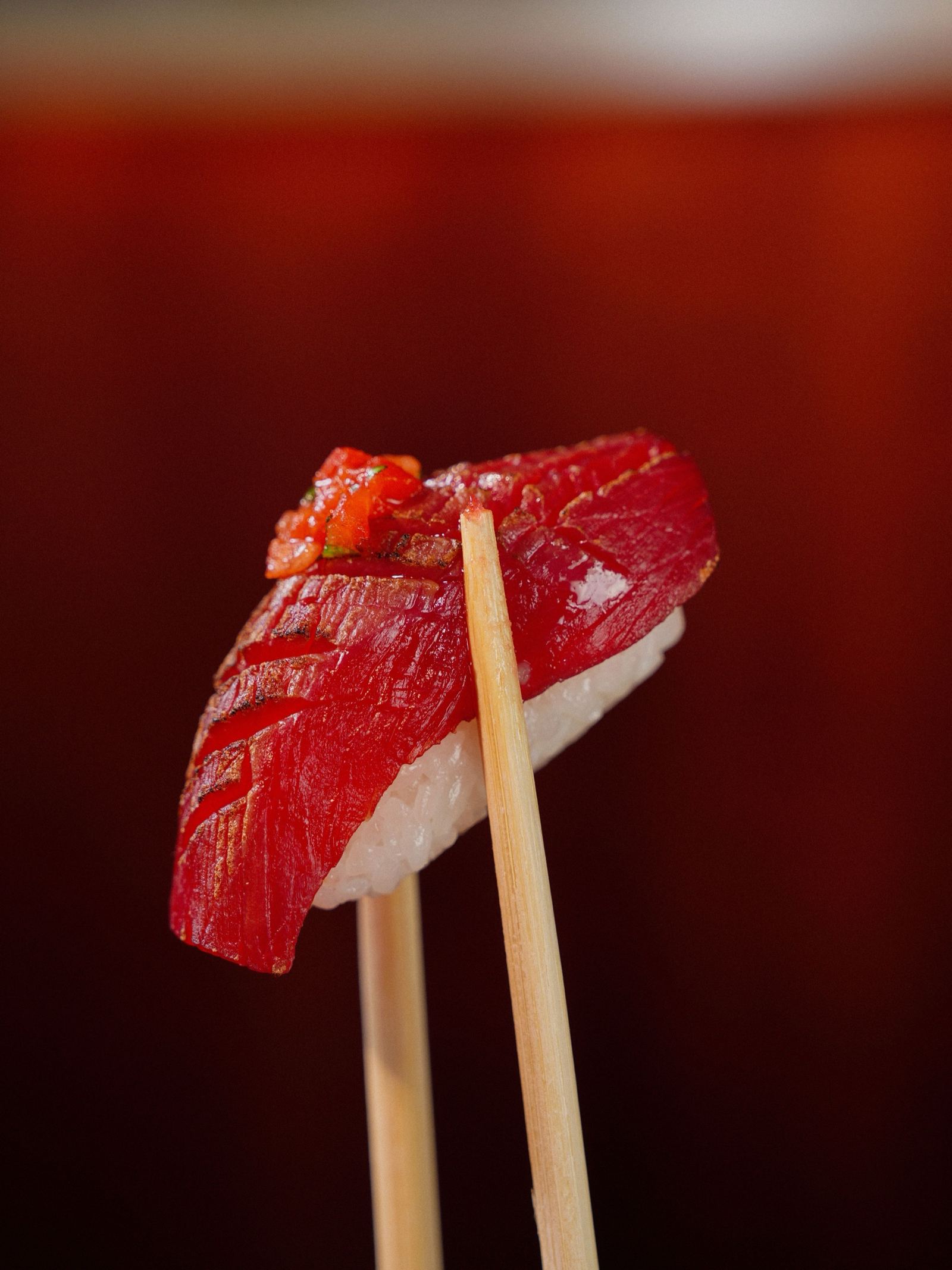 Tonijn-nigiri tussen eetstokjes tegen een rode achtergrond