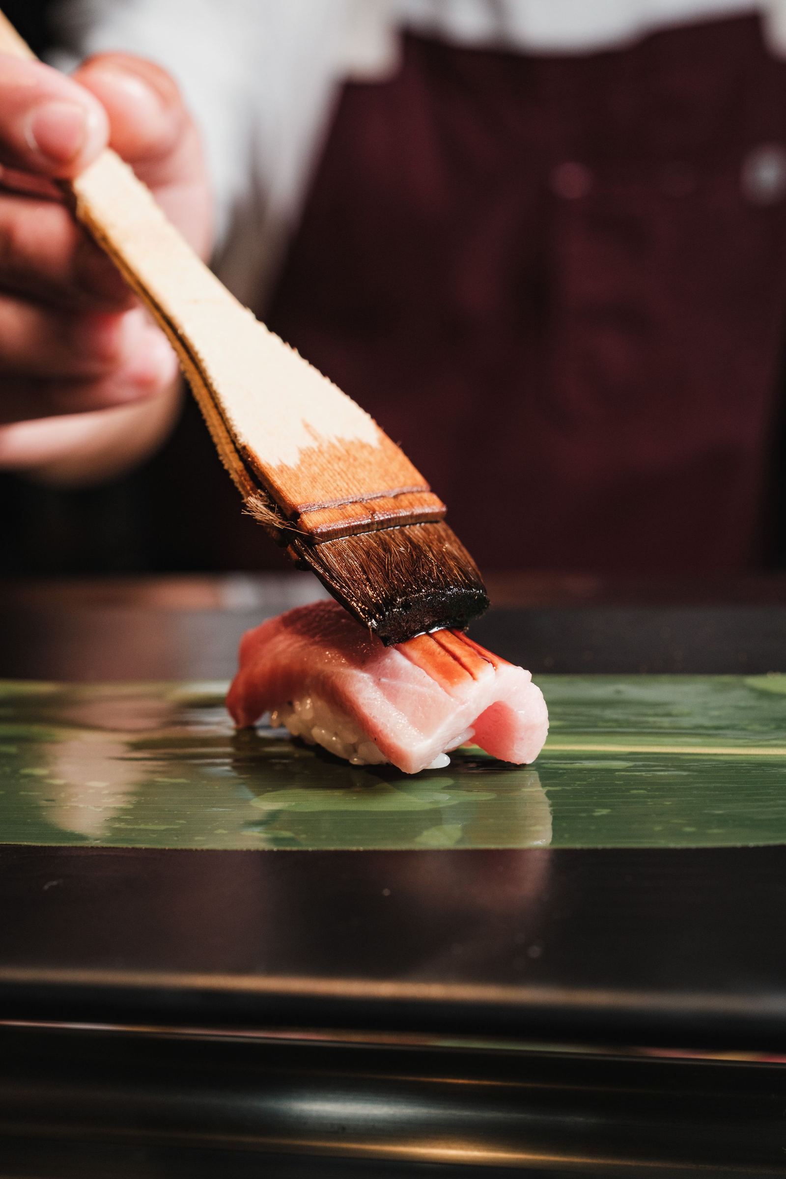 Sushichef glazuurt een nigiri met een kwast