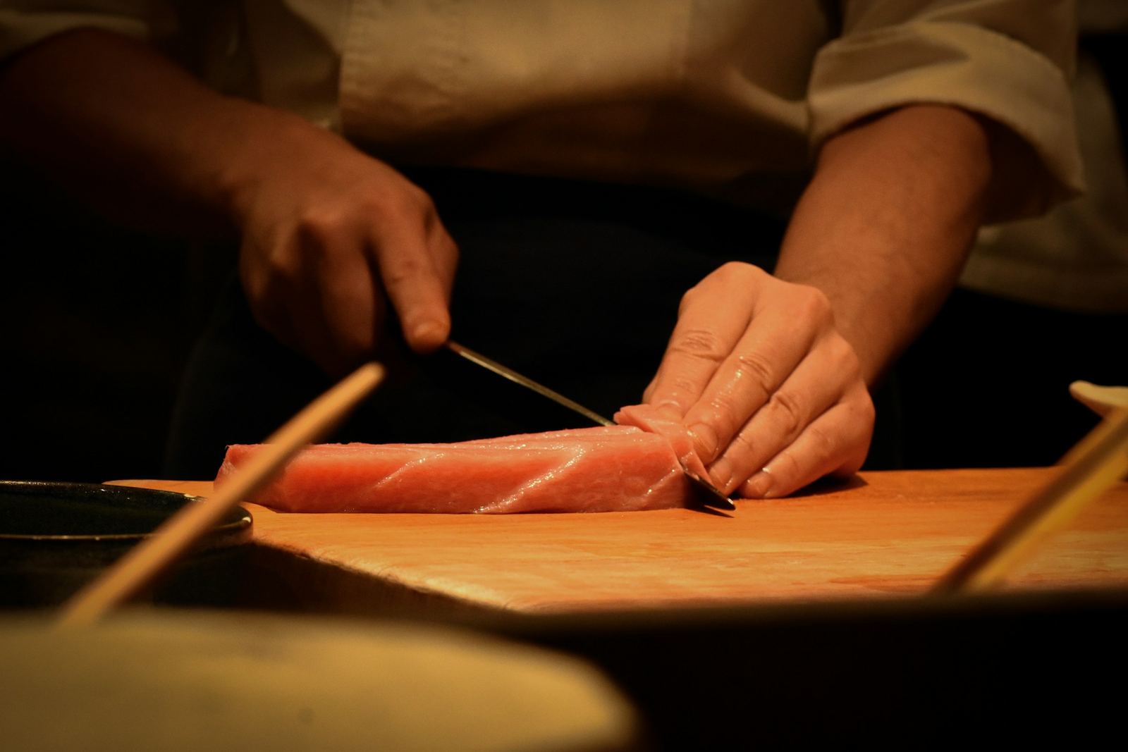 Handen van een sushichef snijden tonijn