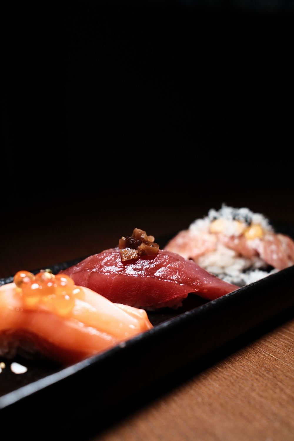 Nigiri met zalm, tonijn en zalmeitjes op een zwarte schaal