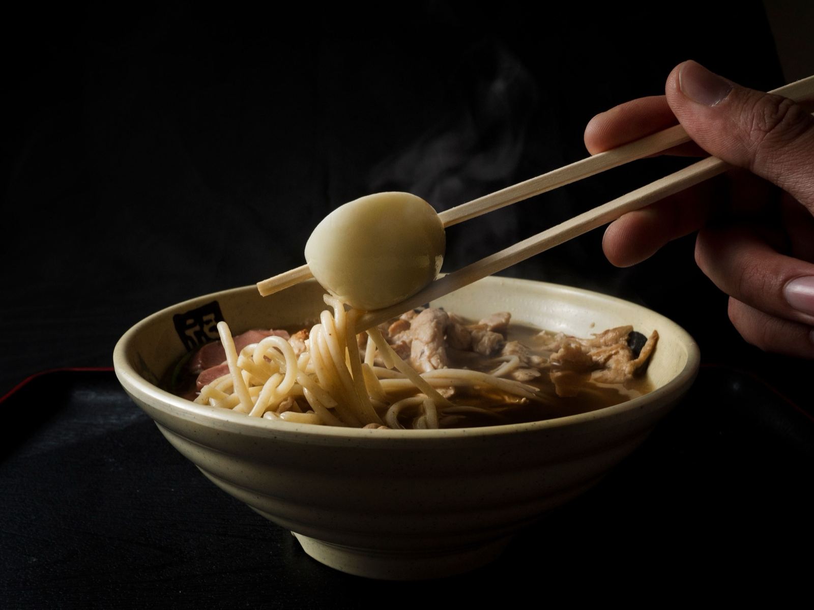 Kom ramen met een ei opgetild door eetstokjes, stoom