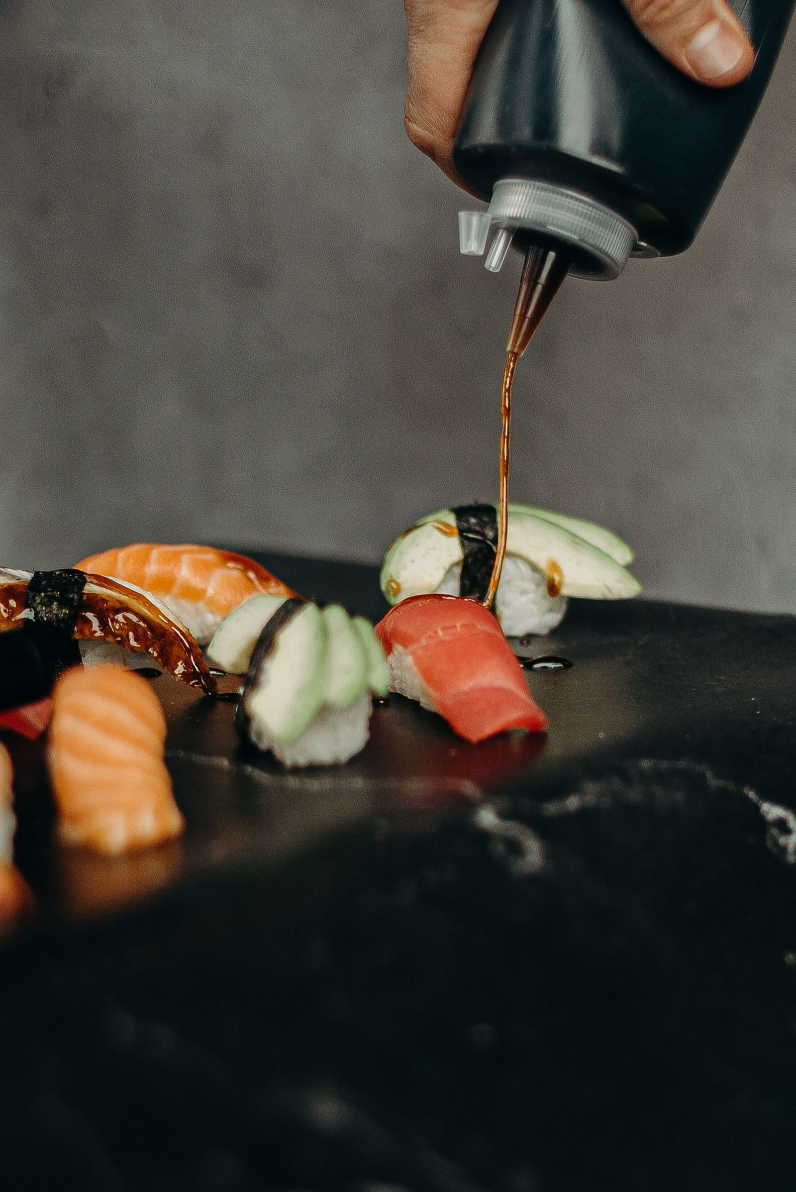 Sojasaus wordt over nigiri gedruppeld op zwart marmer
